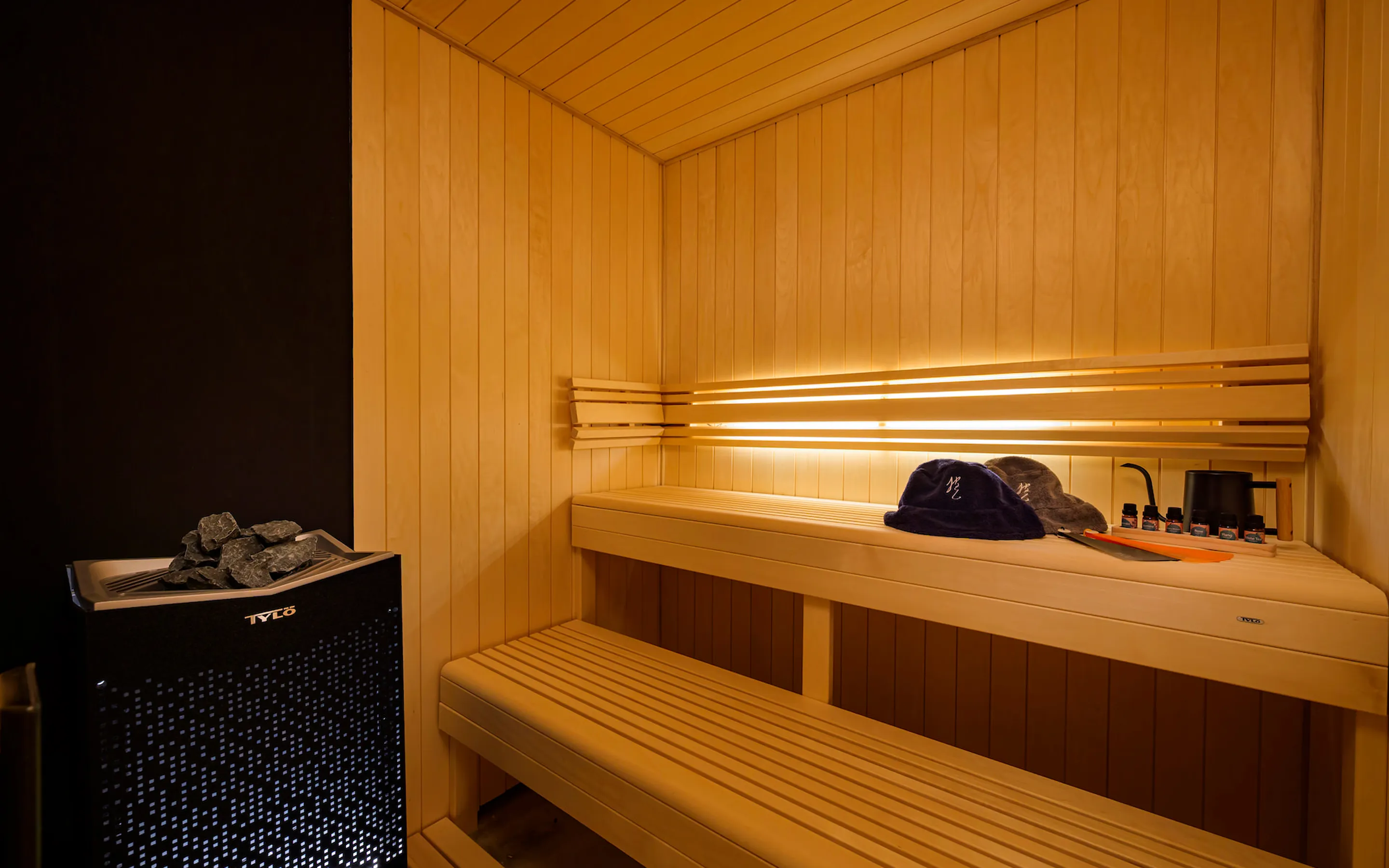 サウナストーンを設置したプライベートサウナ。木製のベンチにサウナハットやアロマオイルが用意されている様子。