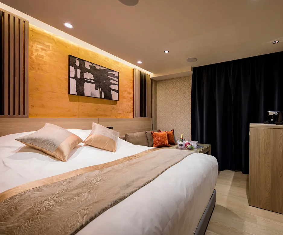 オレンジの間接照明とモノトーンのアートが印象的なダブルルーム。ベッド脇にシャンパンセットが用意されたラグジュアリーな空間